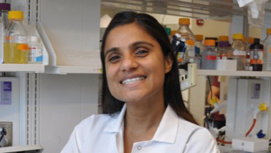 Person smiling with lab equipment in background.