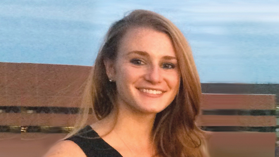 Person with long brown hair in black dress in front of brick building