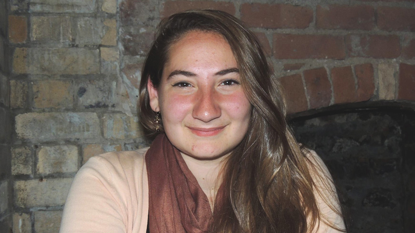 Person with long brown hair in front of fire place.