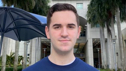 Man with short hair standing by palm trees